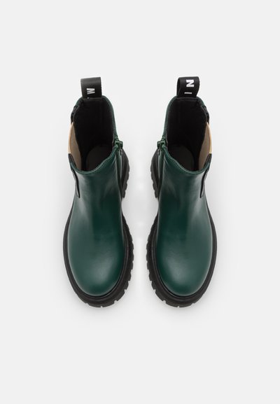 Botas de tornozelo em pele verde com acabamento suave, sola de borracha preta, salto baixo e fecho de zip. Etiqueta em laço na parte de trás para fácil colocação.