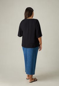 Top corto a maniche corte nero con texture abbinato a una lunga gonna di jeans blu. L'outfit presenta una vestibilità rilassata e un design semplice, con sandali.