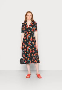 Vestido preto floral com mangas curtas, apresentando flores vermelhas e turquesas. Combinado com sandálias vermelhas e uma pequena mala preta.