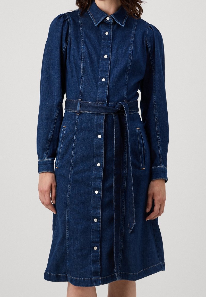 Jeansklänning med långa ärmar, krage, knäppning fram, cinchad midja med bälte, sidofickor och knälängd A-linjeform i mörkblått.