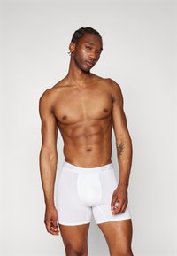 Boxer-chaussettes blanches avec une texture douce et une taille élastique arborant le logo "GAP". La coupe est ajustée, conçue pour le confort et le soutien.