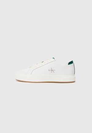 Witte lage Calvin Klein sneakers met crème veters, groene accenten op de hiel en tong, en een lichtbruine zool.