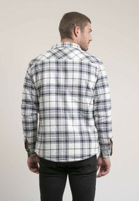 Chemise en flanelle à carreaux blanc et marine avec de longues manches, poignets à boutons et ourlet arrondi. Coutures visibles et col pointed.