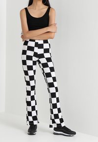 Black tank top paired with white and black checkered flared pants, featuring a sporty design and a comfortable fit, finished with black sneakers.