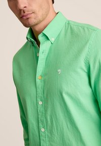 Groene overhemdsblouse gemaakt van gestructureerde stof, met een wit logo en een contrasterende, gemusterde binnenkraag. Standaard pasvorm en kraagontwerp.