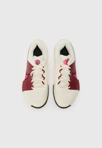 Sneakers with a cream canvas upper, maroon accents, black outsole, and textured design. Features laces and a prominent logo on the sides.