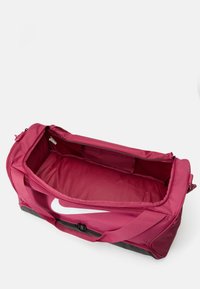 Mala desportiva Nike em tecido rosa escuro com um grande logotipo branco, com fecho de correr e um interior espaçoso, realçada por uma base e alças pretas.