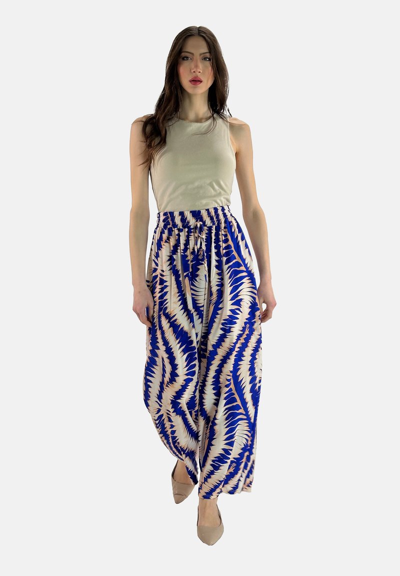 Breda byxor med blå och krämfärgad mönstring och elastisk midja, kombinerat med en åtsittande beige linne och skor i neutrala toner.