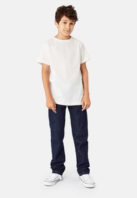 Hvid bomulds t-shirt med korte �ærmer, kombineret med mørkeblå denimjeans. Hvide sneakers fuldender det afslappede outfit med en løs pasform.