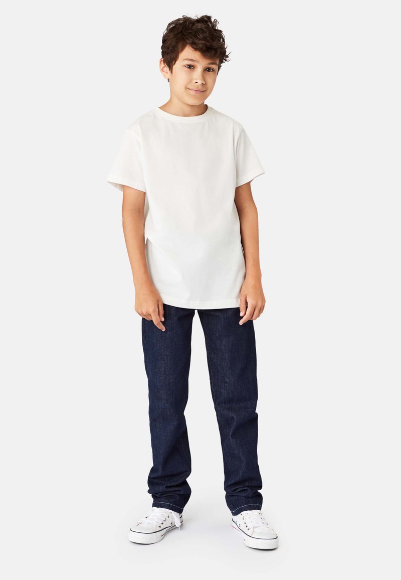 Hvid bomulds t-shirt med korte ærmer, kombineret med mørkeblå denimjeans. Hvide sneakers fuldender det afslappede outfit med en løs pasform.