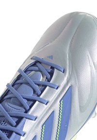 Silver soccer cleat with textured surface, blue laces, and green accent details. Features a tapered design for enhanced performance.