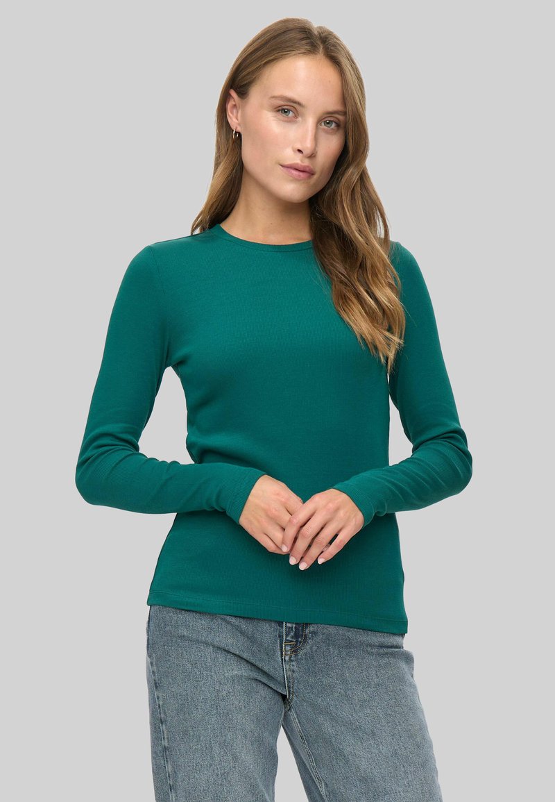 Grünes langärmliges Oberteil aus Rippstoff, mit runder Halslinie und schmaler Passform, kombiniert mit hoch taillierten blauen Jeans.