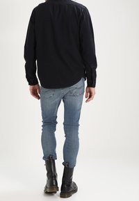 Maglietta nera a maniche lunghe con orlo curvo, abbinata a jeans skinny azzurri chiari e stivaletti neri alla caviglia. Dettagli notevoli includono le cuciture e gli accessori metallici.