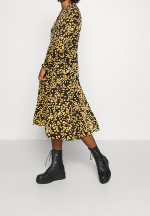 Czarna sukienka w kwiaty z żółtymi kwiatami, długimi rękawami i rozkloszowanym dołem, zestawiona z czarnymi platformami na sznurowane botki.