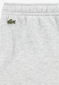 Grå joggebukser laget av myk bomullsblanding, med elastisk midje og en liten grønn krokodillelogo sydd på venstre side.