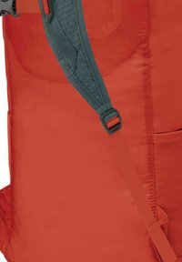 Zaino rosso con un tessuto liscio e resistente, dotato di una tracolla con un pad grigio texturizzato e una fibbia regolabile. Tasca laterale visibile.