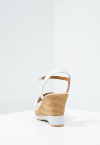 Bílé wedges sandály s propleteným juteovým podpatkem a hladkým bílým podložím. Mají páskový design a nastavitelné sponky na kotníku.