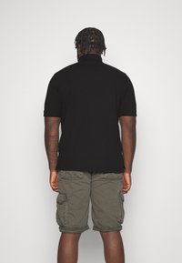 Černé polo tričko s krátkým rukávem a klasickým límečkem, v kombinaci s olivově zelenými cargo šortkami, které mají boční kapsy a volný střih.