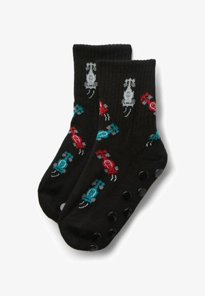 Schwarze Socken mit roten, blauen und grauen Rennwagenmustern und schwarzen rutschfesten Grip-Punkten auf den Sohlen, gefaltet vor weißem Hintergrund.