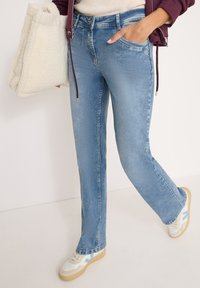 Niebieskie dżinsy z prostymi nogawkami, z klasycznym pięciopocketowym designem, w połączeniu z torbą z sztucznego futra w kolorze kremowym i beżowymi trampkami.