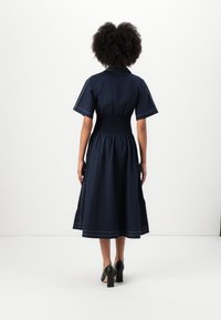 Vestido de algodão azul-marinho com mangas curtas, cintura ajustada e saia evasê. Apresenta costura branca em contraste e comprimento até ao joelho.