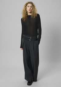 Čierny rebrovaný top s dlhým rukávom a zapínaním na gombíky, kombinovaný s tmavosivými širokými nohavicami, ktoré majú dvojitý prackový pás a plisovanú prednú časť.