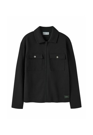 Veste noire zippée avec manches longues, deux poches poitrine à rabats avec boutons, et un col, présentée sur fond blanc.