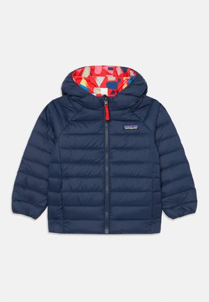 Sötétkék puffdzseki piros béléssel, színes geometrikus mintával, elöl cipzáros záródással és elasztikus mandzsettákkal.