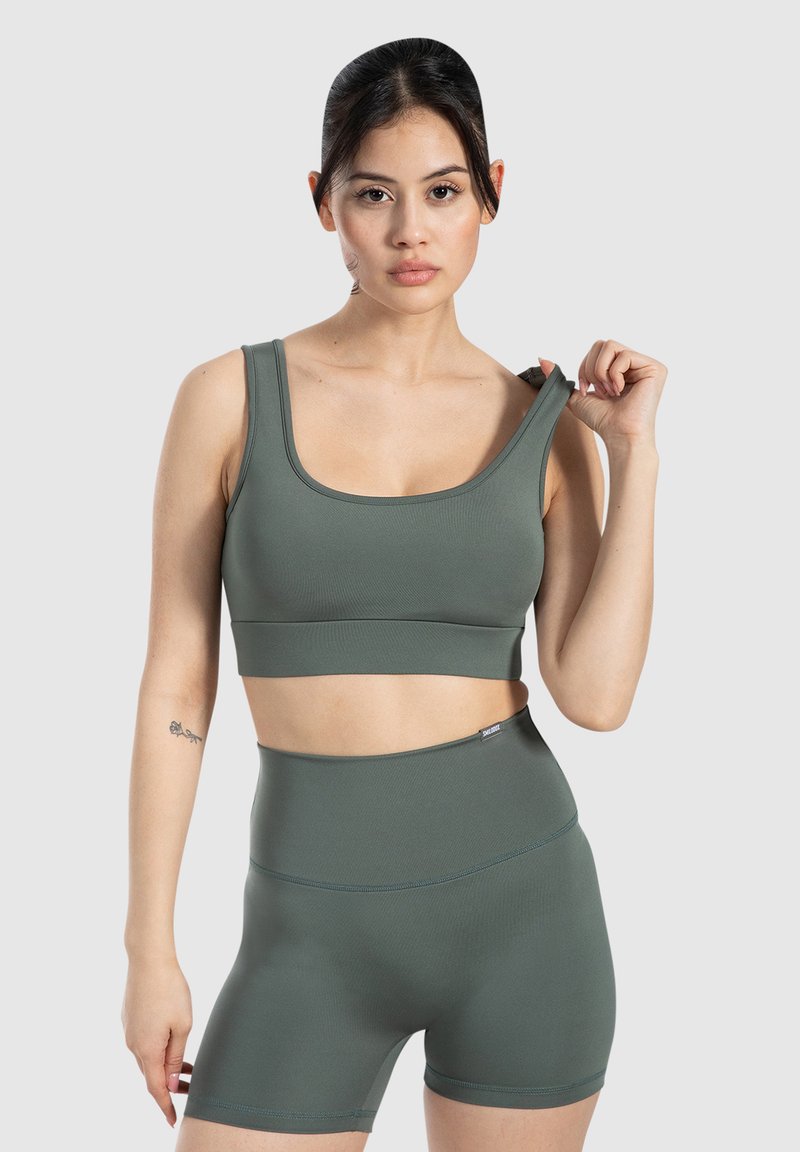 Top de deporte y pantalones cortos de tiro alto en un tono verde apagado, hechos de una tela texturizada y elástica con tirantes anchos y detalles sutiles del logo.