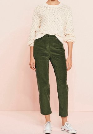 Lyscreme strikket sweater med tekstureret mønster, parret med olivengrønne kordbukser med lige snit, iført en model med hvide sneakers.