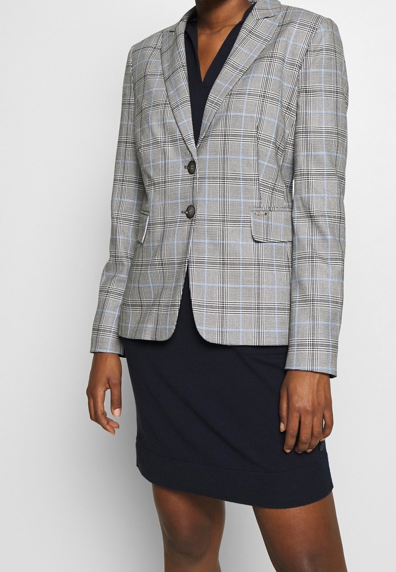 Blazer de cuadros en gris con líneas azul claro, que presenta dos botones, solapa con muesca y dos bolsillos delanteros, llevado sobre un vestido oscuro.
