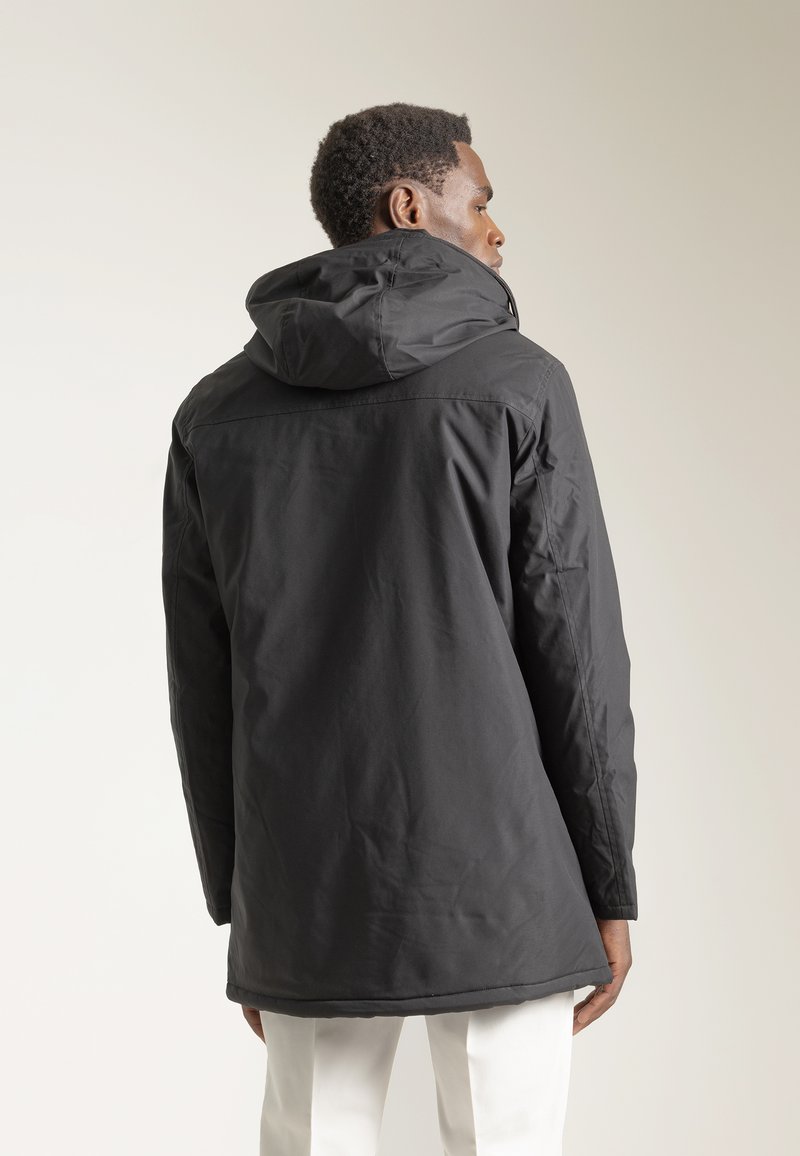 Chaqueta impermeable negra con capucha, que presenta una textura suave, silueta recta y dobladillo trasero más largo para mayor cobertura.