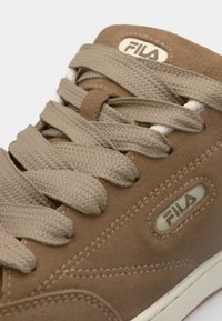 Baskets en suède beige avec des lacets plats beiges, des accents blancs et un patch du logo Fila. Dotées de détails cousus et d'une surface texturée.