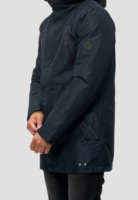 Námořnická parka s voděodolnou tkaninou, zipovými náprsními kapsami, nastavitelnou kapucí a žlutými akcentovými detaily na lemu a rukávech.