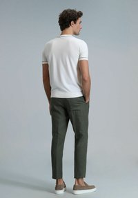 Weißes Poloshirt mit kurzen Ärmeln und geripptem Ausschnitt, kombiniert mit schmal geschnittenen grünen Hose und hellbraunen Slippern.