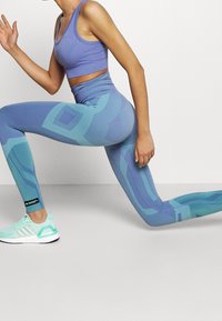 Ljust lila sport-bh och matchande leggings med geometriska blå mönster, tillverkade av stretchigt material. Skor med mintgrön design.