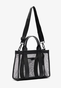 Saco tote preto com painéis de malha transparente e acabamentos em pele preta, apresentando duas alças e uma alça de ombro destacável.
