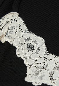 Tessuto nero con delicata bordatura in pizzo bianco, che mostra un motivo floreale intricata con bordi ondulati, offrendo un contrasto di texture.