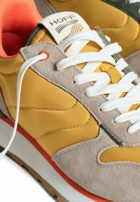 Sneakers met een mix van gele synthetische materialen en grijssuede, witte veters en een groene accent, met een oranje zooldetail.