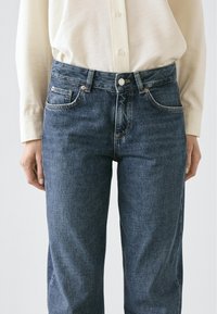 Ciemnoniebieskie dżinsy z prostą nogawką, posiadające przednie kieszenie, zapięcie na guzik oraz subtelne detale szwów.