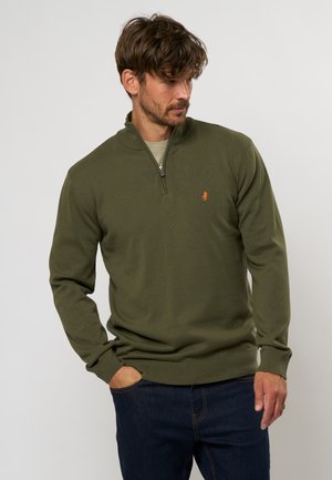 Pull olive vert à manches longues avec un col zippé mi-long, en tissu tricoté texturé, et petit logo brodé sur la poitrine. Assorti à un jean foncé.