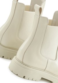 Kremasto-bež kožne Chelsea čizme s elastičnim bočnim panelima, čvrstim gumenim potplatom i šivenim detaljima na šavovima.
