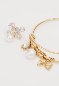 Ensemble de bijoux en métal doré avec des accents en perles, des boucles d'oreilles en forme de papillon en cristal et un bracelet avec un charme en forme de nœud et un détail en cristal en goutte.