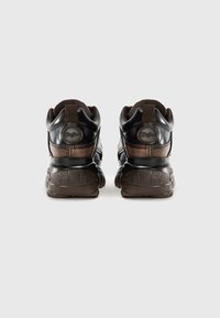 Sapatilhas de couro castanho com uma sola texturizada de castanho escuro, colarinho acolchoado e um emblema de marca na parte de trás. Apresenta um design robusto.