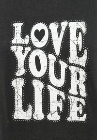 Μαύρο βαμβακερό T-shirt με μεγάλα ραγισμένα λευκά γράμματα που αναγράφουν «LOVE YOUR LIFE» με μια μικρή λεπτομέρεια καρδιάς και διακοσμητικές κουκκίδες.