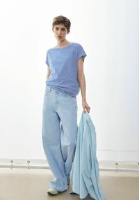 Gestreept blauw-wit T-shirt met korte mouwen, lichtblauwe wijde jeans, houdt een lichtblauw overhemd vast. Soepele stof, casual pasvorm.