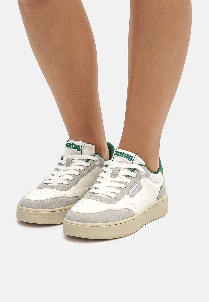 Baskets blanches et grises avec une finition en daim, arborant des accents verts, un collier rembourré et des lacets, conçues pour un usage décontracté.