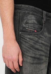 Μαύρο ξεθωριασμένο τζιν με στενή εφαρμογή, διαθέτοντας μπροστινή τσέπη με ορατή ετικέτα και αντίθετη ραφή κατά μήκος των ραφών.