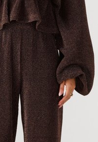 Bruine ribgebreide outfit met een textuurtop met ruches en brede mouwen, gecombineerd met bijpassende broeken met een vergelijkbaar patroon.