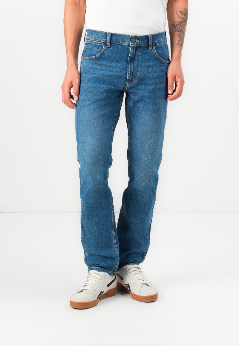 Blauwe denim jeans met een rechte pasvorm, vijf-pocket ontwerp, klassieke stiksels en een bijpassende knoopsluiting, gecombineerd met witte sneakers.